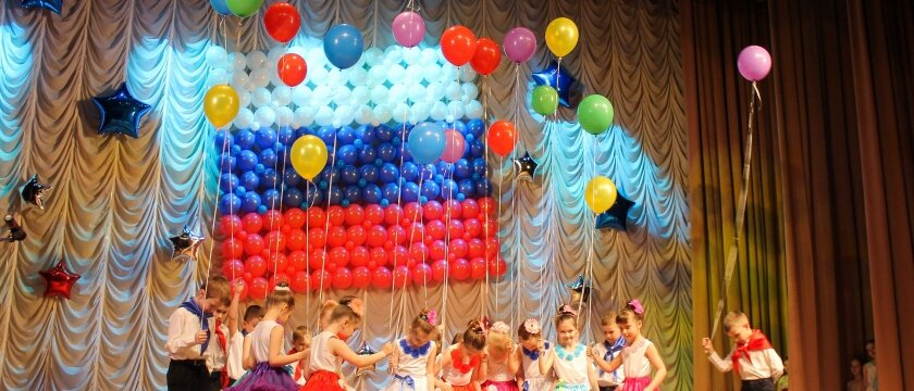 Концерт в ДК 1 июня 2015 года, дети с шариками в руках кланяются, им аплодируют, на фоне флаг России из шариков