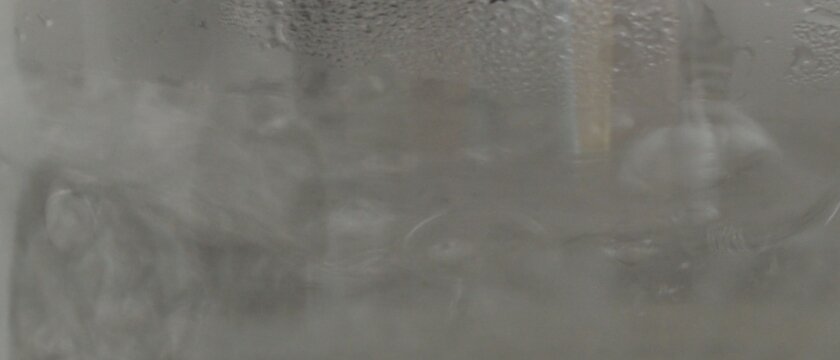 Кипящая за стеклом вода, сверху капли конденсированной воды, мутная картинка