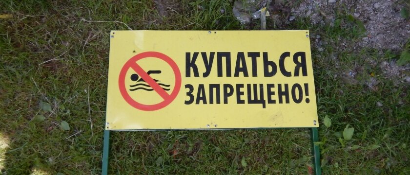 Табличка «Купаться запрещено», желтая табличка и знак запрета купания, валяется на траве и земле, Московская область