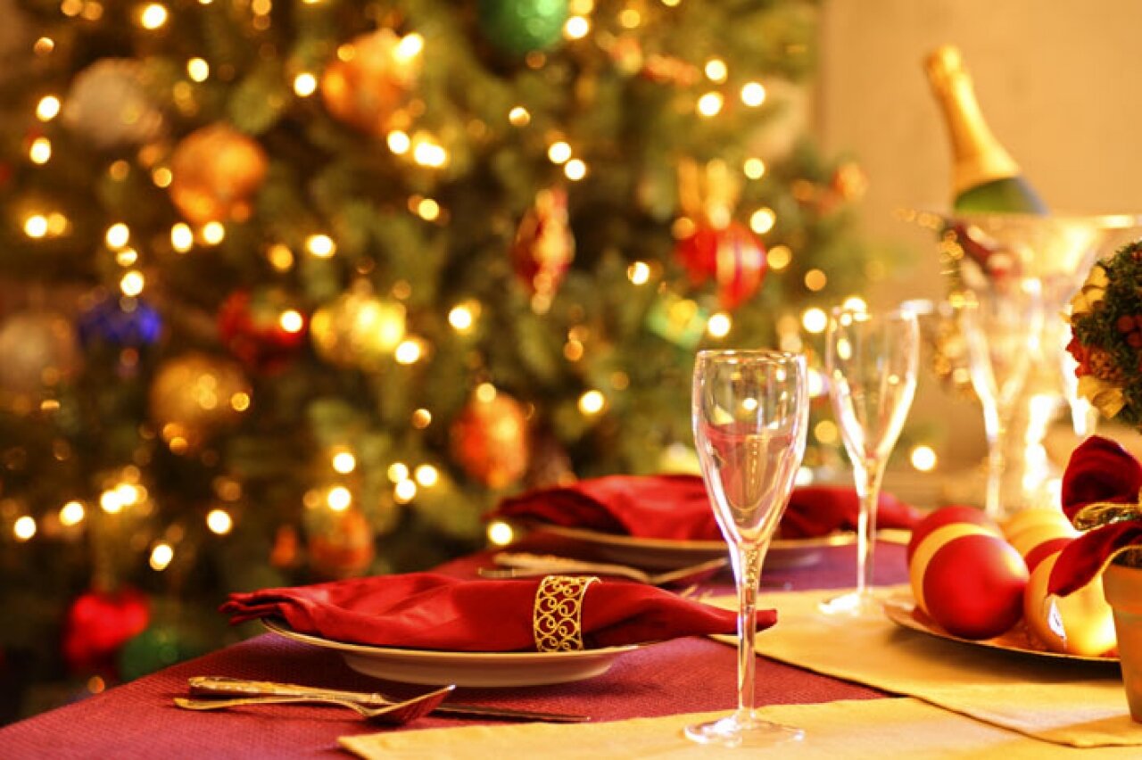 Праздничный новогодний стол, стоят бокалы с шампанским, на заднем плане украшенная ёлка